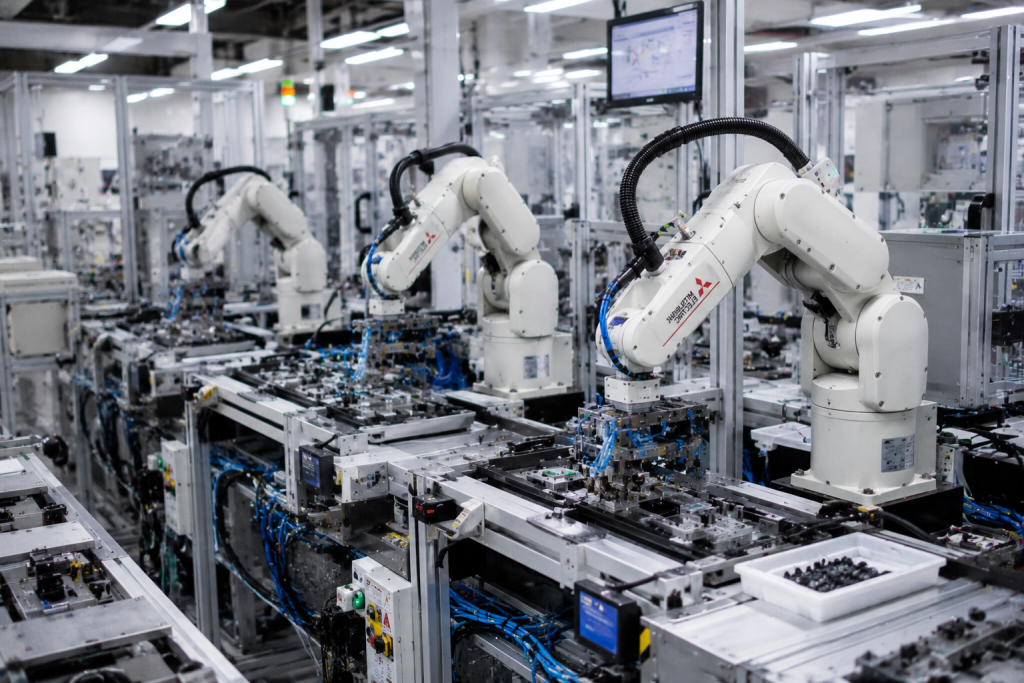 small white robots in an assembly line with small parts on a conveyer.